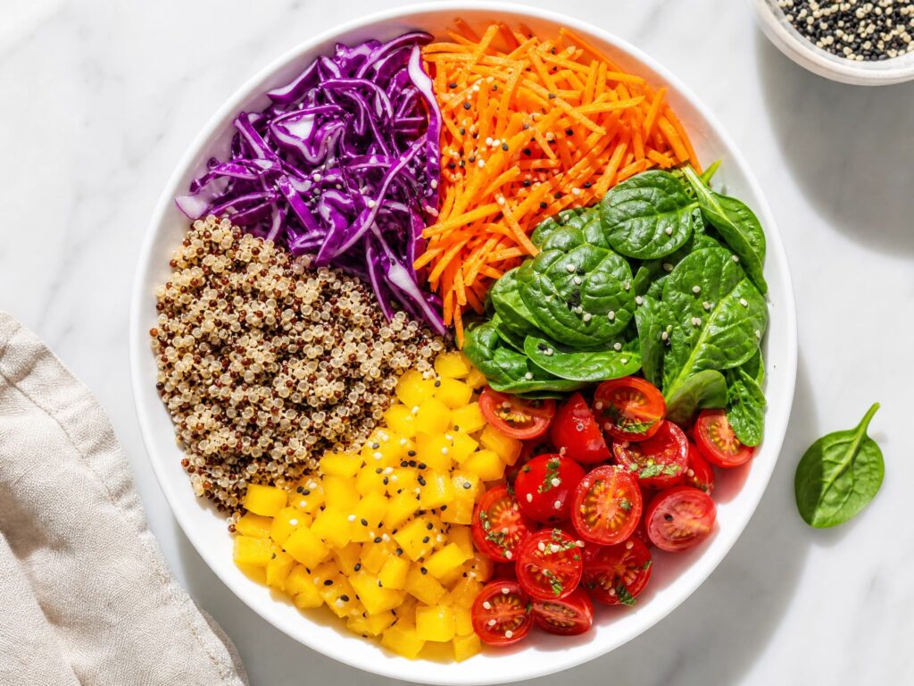 Prato branco com divisões coloridas de vegetais roxos, laranjas, verdes, vermelhos e amarelos, representando a variedade nutricional.